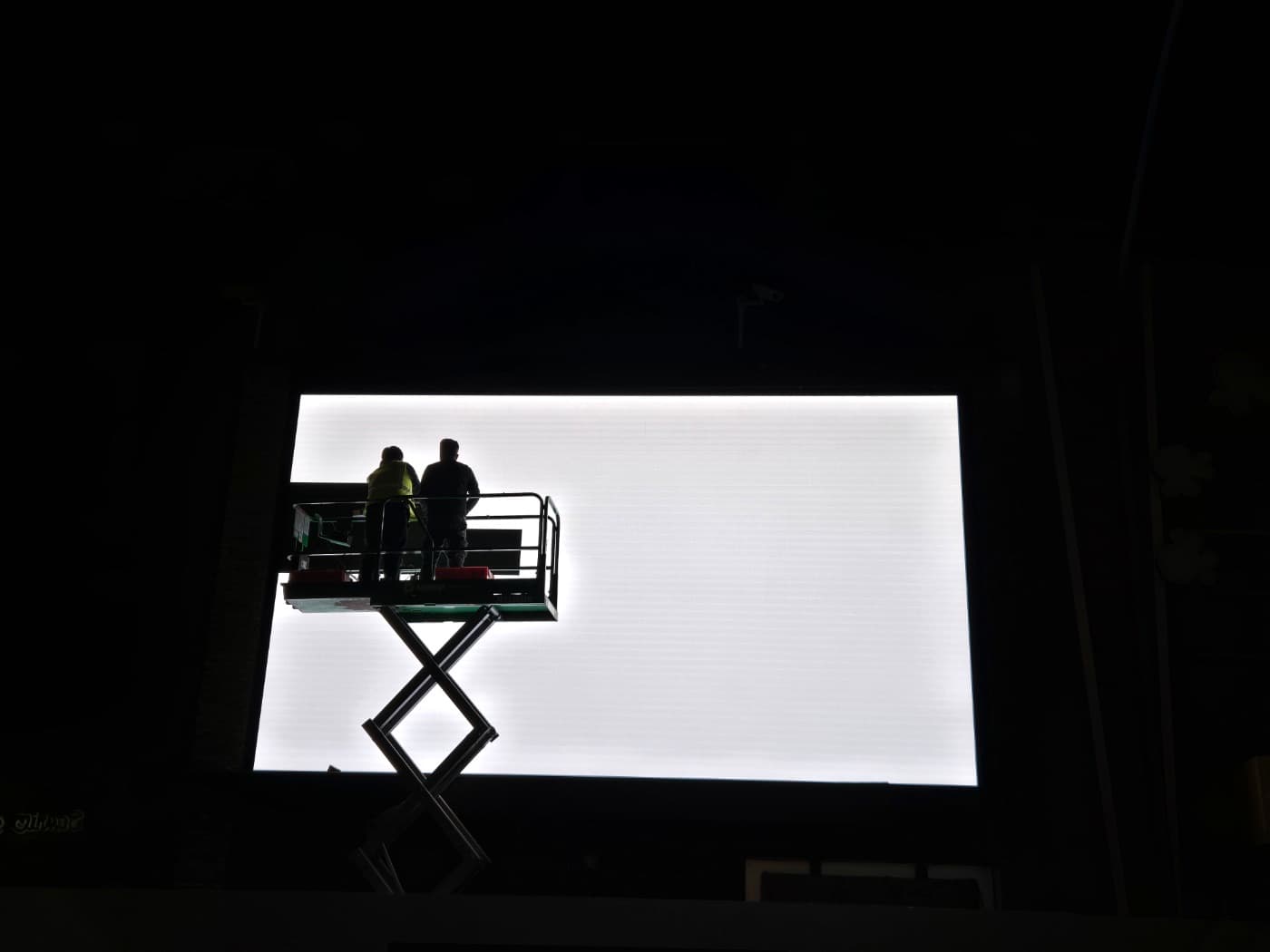 Crew on a scissor lift installing a large-format LED display at night