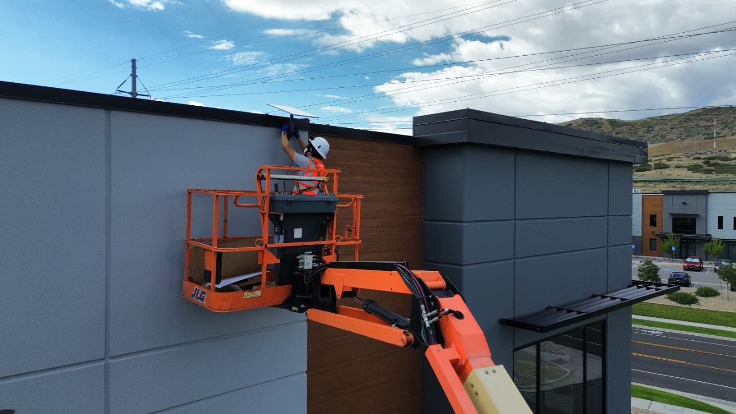 Technician mounting rooftop equipment at a building corner