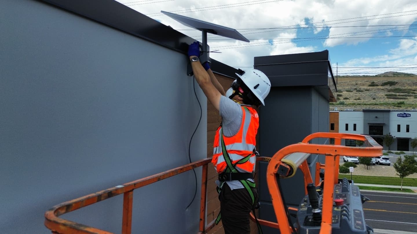 Technician on a boom lift mounting a wireless access point to a rooftop parapet